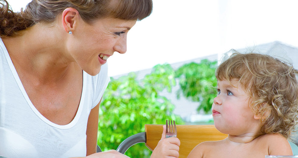 A woman and a child sit at a table, with the child holding a fork.