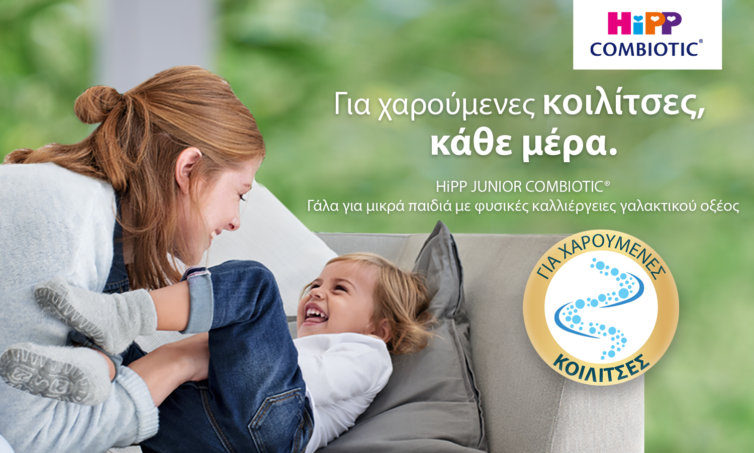 Μια γυναίκα και ένα γελαστό παιδί απεικονίζονται σε έναν καναπέ, με ένα λογότυπο και ένα κείμενο που διαφημίζει ένα προϊόν που ονομάζεται "HIpp JUNIOR COMBIOTIC®".